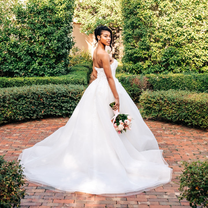 Woman in a white wedding dress holding flowers in an outdoor setting with greenery.